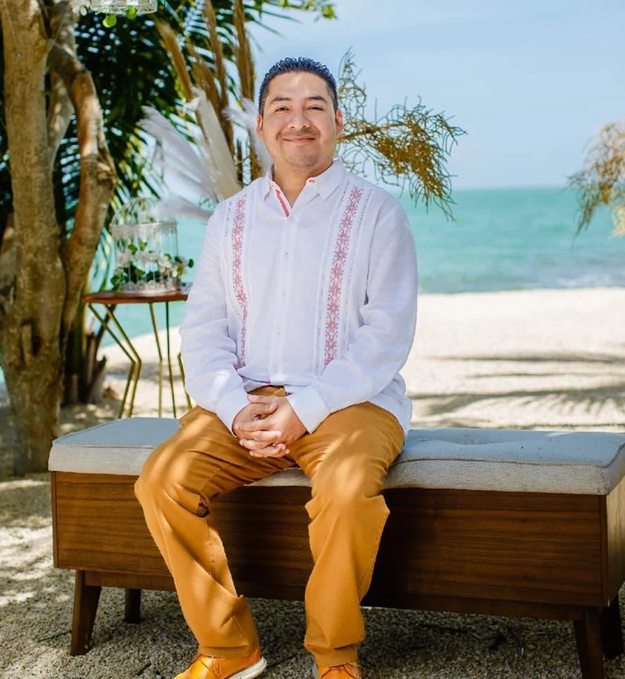 Josué Osmany, con guayabera blanca, sentado frente al mar